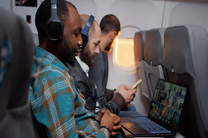 Entrepreneur talking on videocall conference on airplane flying in economy class. Using online remote teleconference call on laptop, travelling with internet meeting.