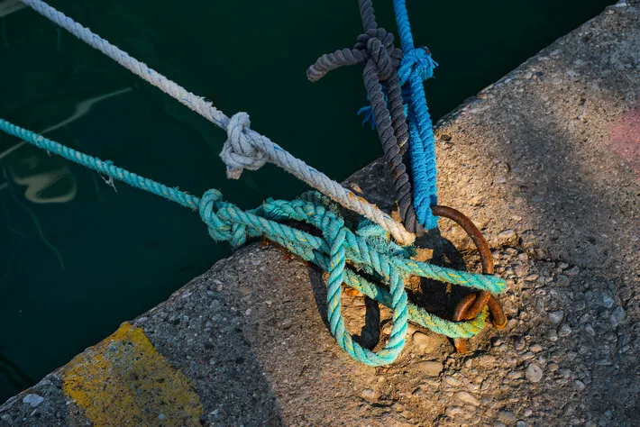Mooring ring with tied blue and white nautical rope mounted on a concrete pier, marina safety equipment